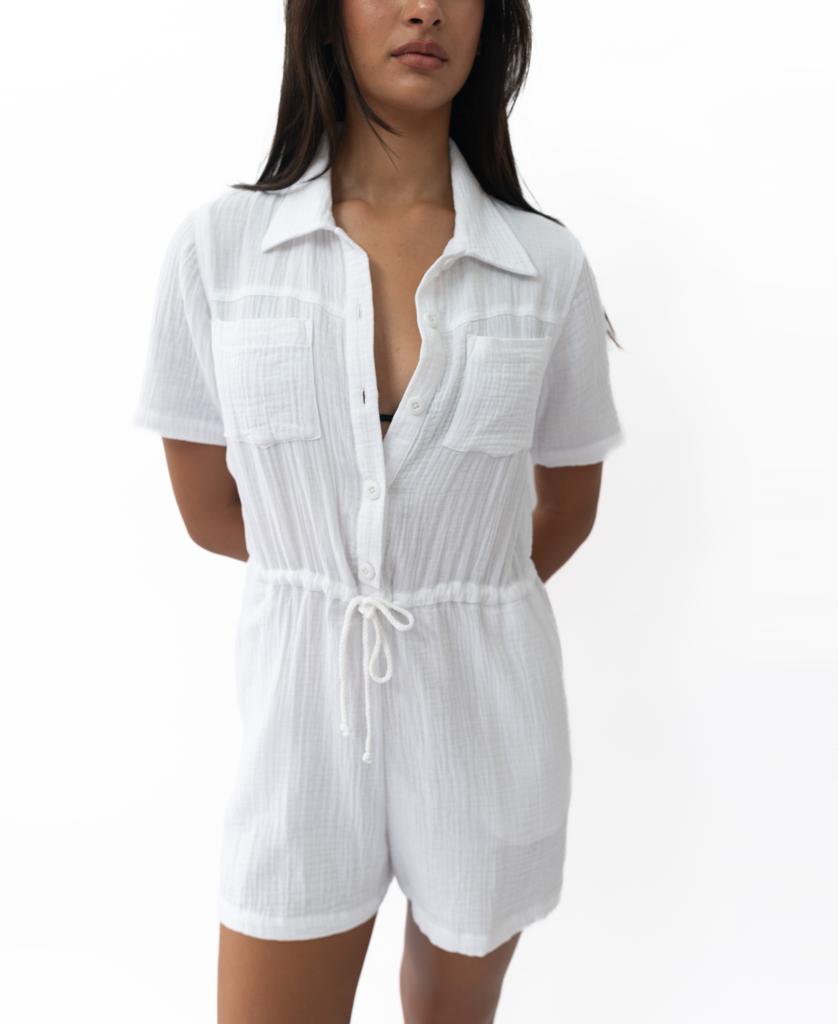 A woman models the Golden Breed Lexi Playsuit | White, a soft cotton-blend short-sleeve button-up romper with a drawstring waist, against a plain white background.