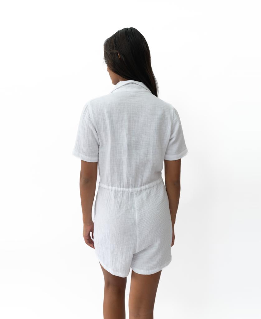 A person stands with their back to the camera, wearing the Golden Breed Lexi Playsuit | White, crafted from a soft cotton blend, set against a plain white background.