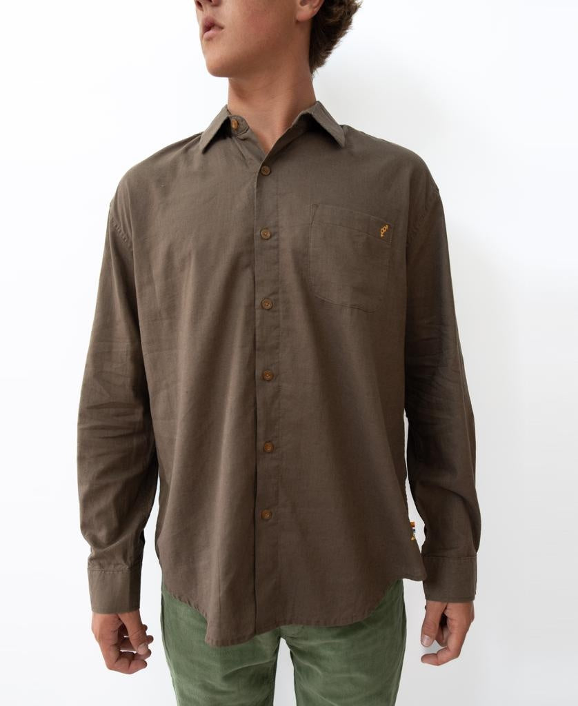A person wears the Golden Breed Linen LS Shirt in Wash Brown with a chest pocket, paired with green pants, standing against a plain white background.