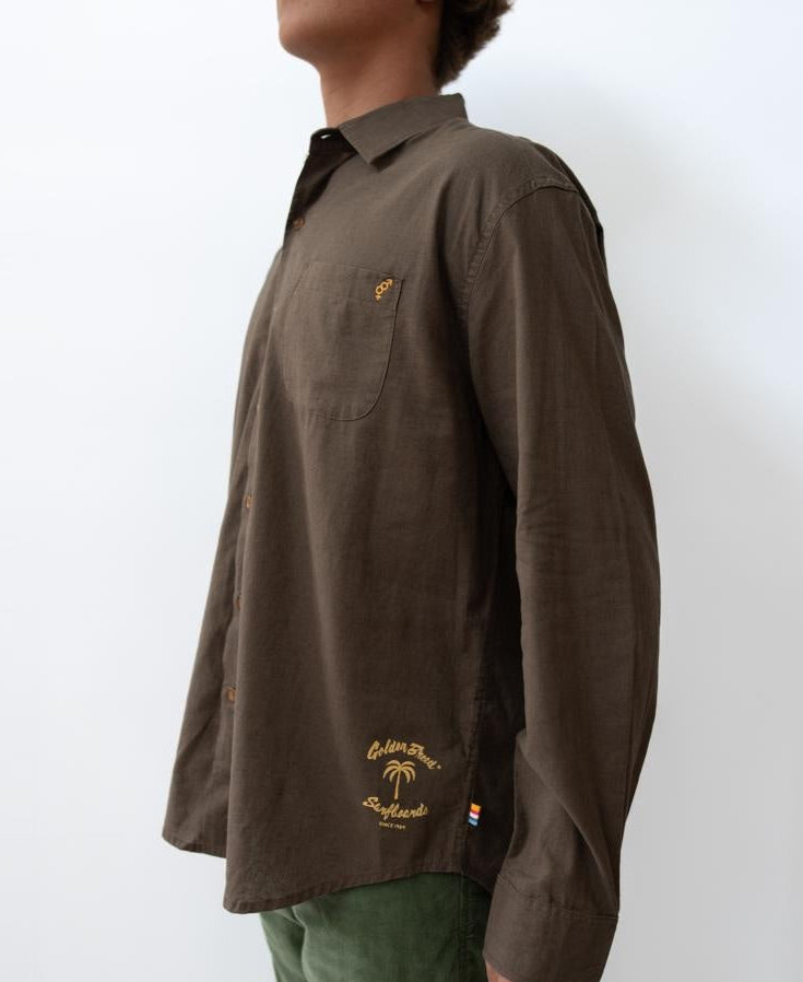 A person wearing a Golden Breed Linen LS Shirt | Wash Brown, featuring yellow embroidery on the pocket and hem, stands against a plain white background.