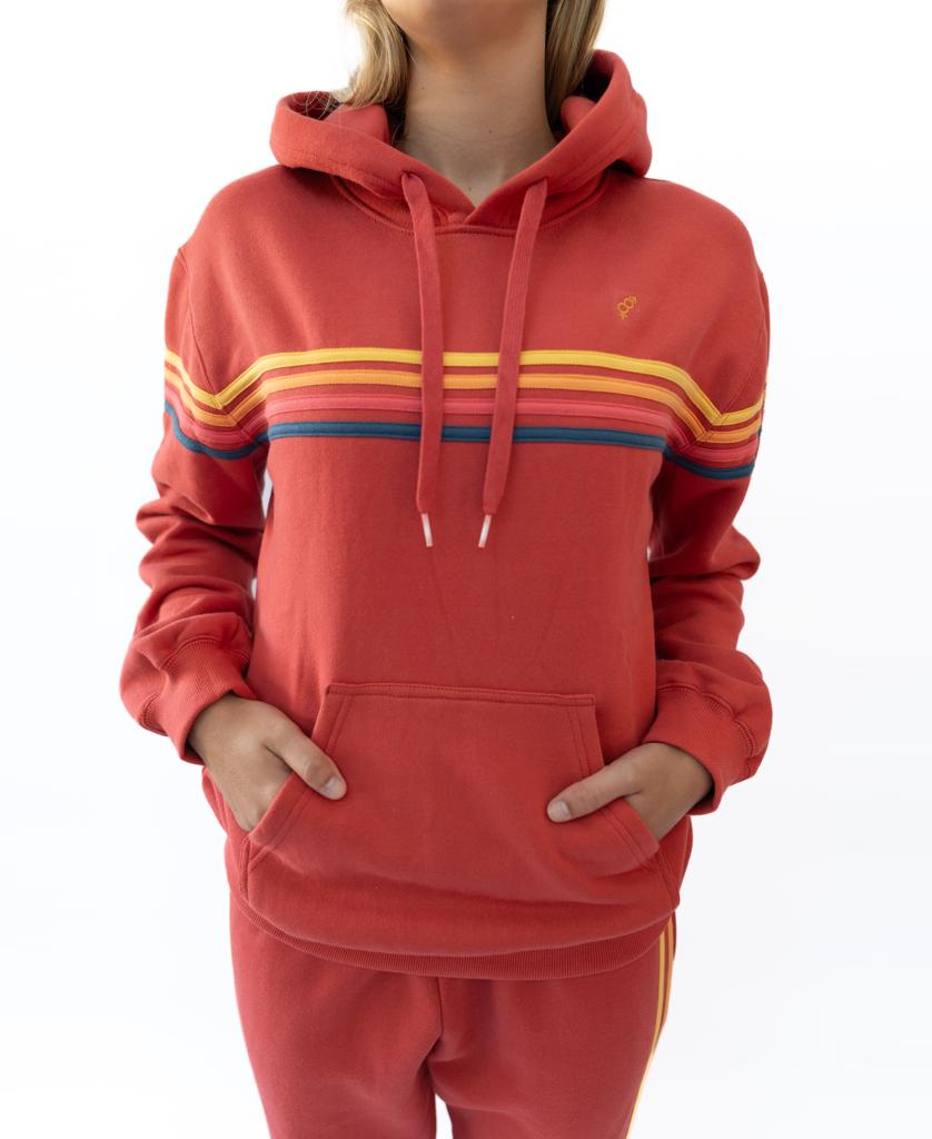 A person wears the Golden Breed Long Island Hoodie | Wash Red, featuring yellow, orange, and blue chest stripes and a front pocket. Matching red pants are also visible. The hoodie is made from 100% cotton fleece.
