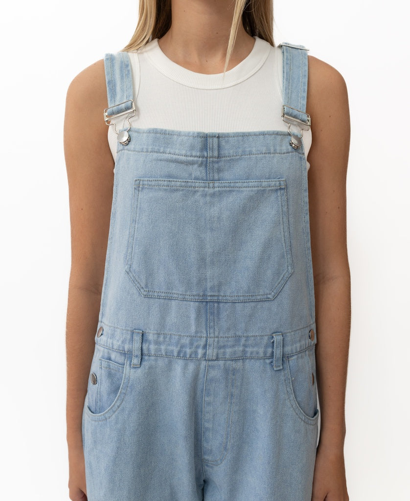 A person models the Golden Breed Maci Overall in light blue—handmade denim with adjustable straps—over a white ribbed sleeveless top, shown from shoulders to waist against a plain white background.