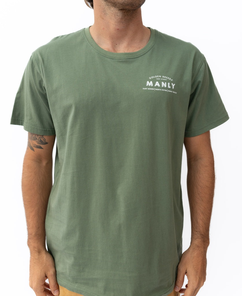 A man wears a khaki Manly Old School Tee by Golden Breed, featuring white MANLY text on the left chest, standing against a white background.