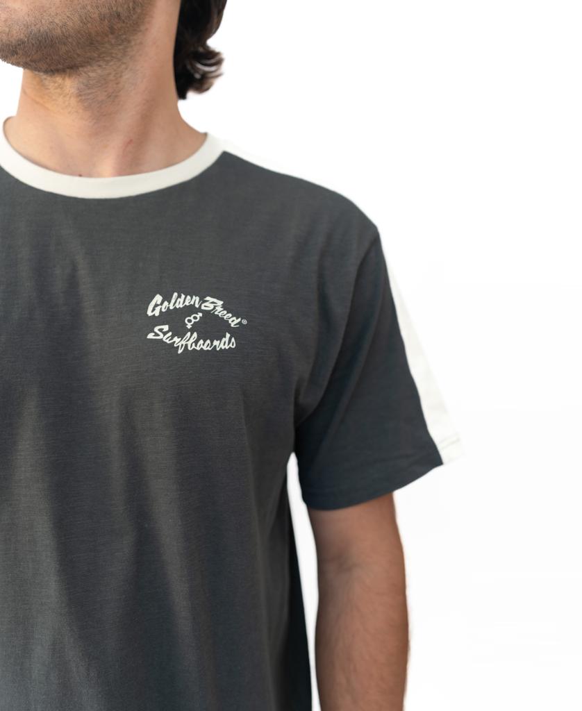 A person in a Golden Breed Mitch Tee | Wash Black, featuring white trim and a Golden Bones Surfboards logo on the left chest, echoing classic Golden Breed style.