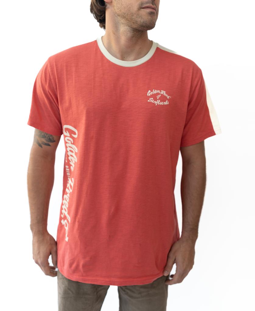 A man stands against a white background wearing the Golden Breed Mitch Tee in Wash Red, featuring white text on the chest and side, paired with brown pants.