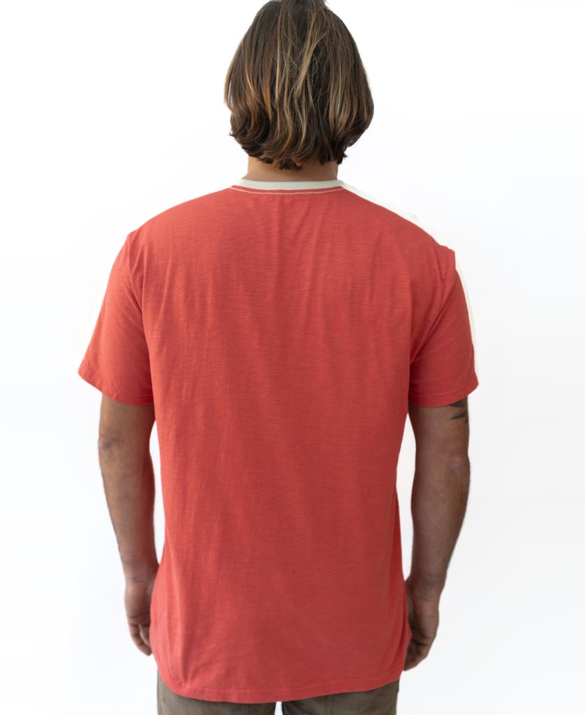 A person with shoulder-length hair faces away, wearing the Golden Breed Mitch Tee in Wash Red (short sleeves, cotton slub) and brown pants against a plain white background.