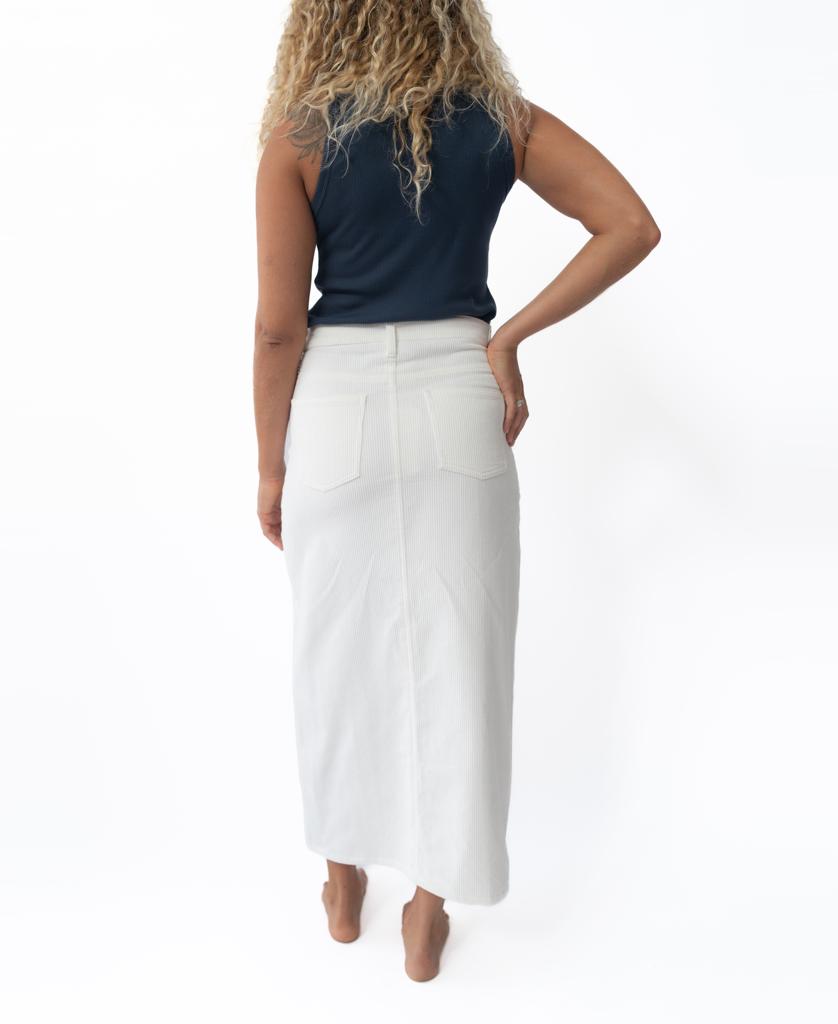 A person with curly hair stands barefoot, facing away, wearing a navy sleeveless top and the Golden Breed Nellie Maxi skirt in Off White with back pockets, Handmade in Indonesia, against a plain white background.
