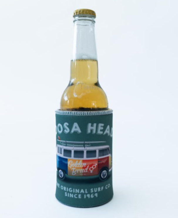 A clear glass bottle with golden liquid rests in a Golden Breed Noosa Stubby Kombi | Surf Green holder, featuring a colorful van illustration and “Golden Breed” branding.