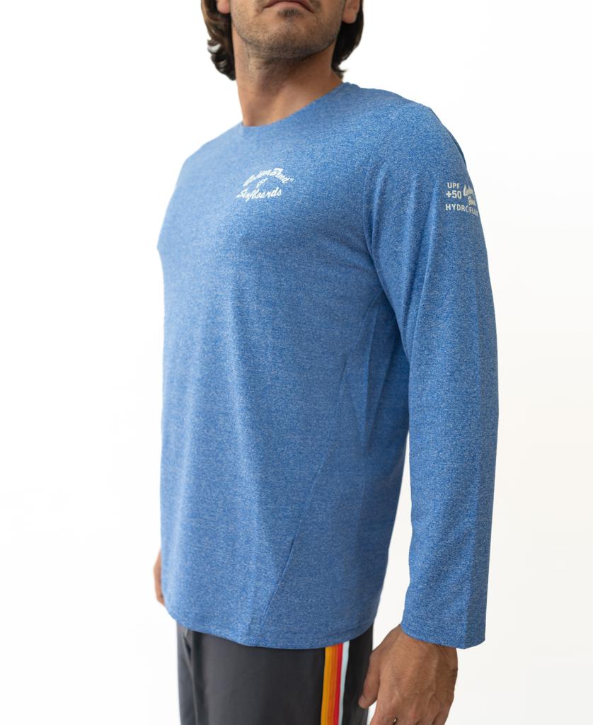 A man stands against a plain white background wearing the Golden Breed Pebbles L/S Rash Shirt in Blue Marle, featuring UPF 50+ protection and white chest and sleeve text, paired with black shorts with red and yellow side stripes.