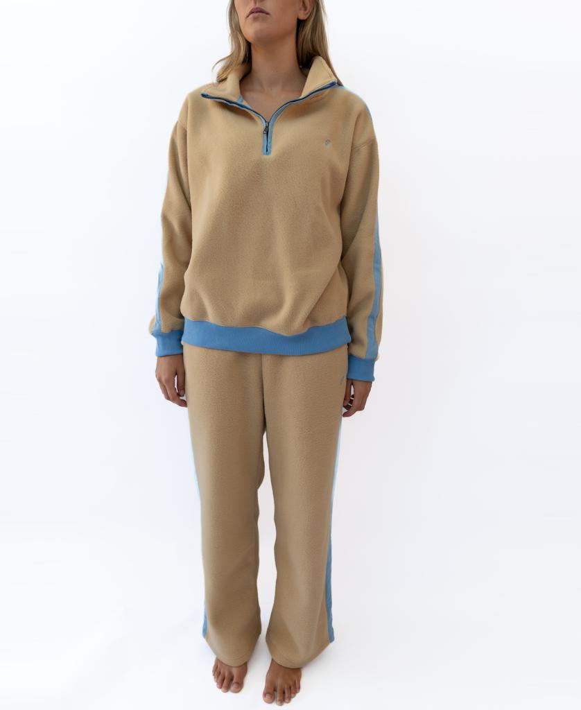 A person stands barefoot in the Golden Breed Peggy 1/2 Zip Retro tracksuit in Beige/Azure, featuring blue trim and the iconic logo, against a plain white background.