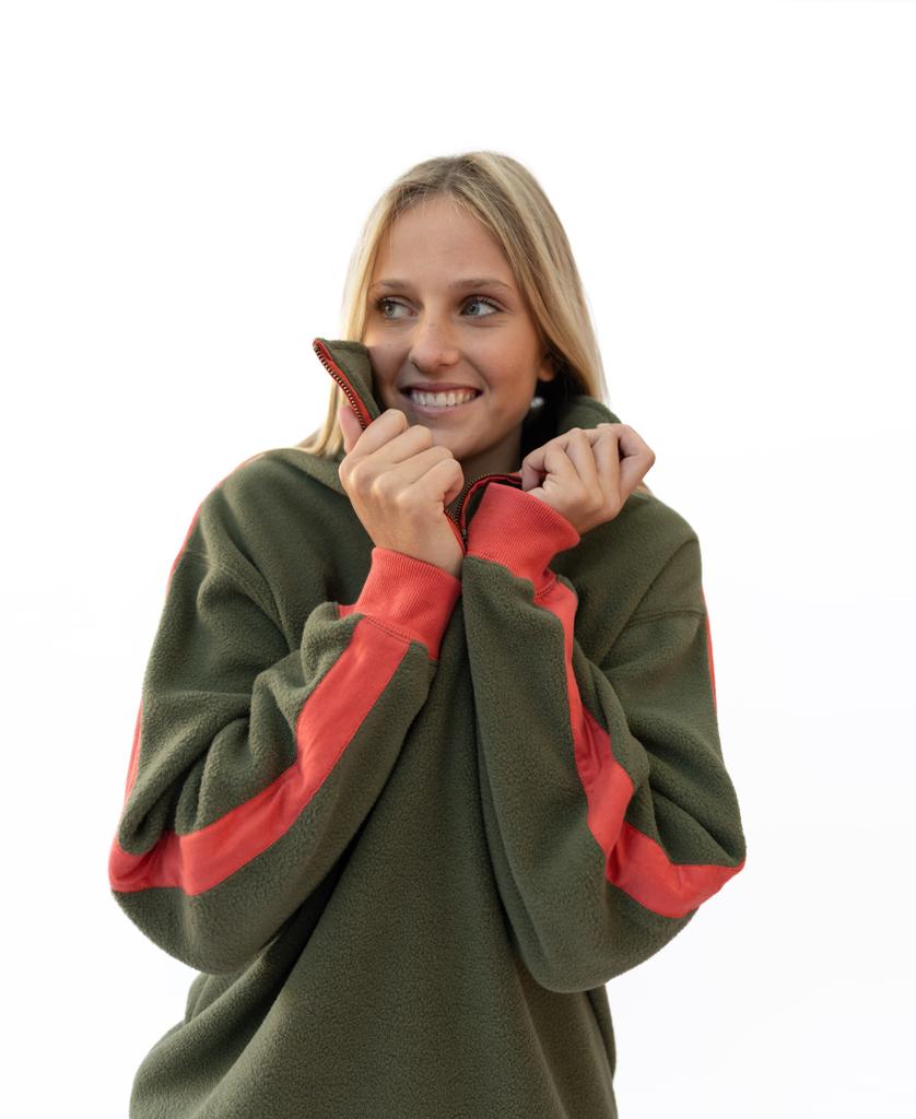 A woman smiles while holding the collar of her Peggy 1/2 Zip Retro fleece in Dk Khaki/Red by Golden Breed against a white background.