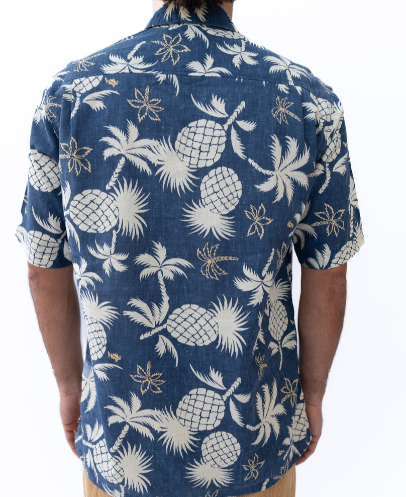 A man seen from behind wears the Pine-Palm Reverse Shirt in Vintage Navy by Golden Breed, an oversized relaxed-fit cotton-linen shirt with white pine palm and floral prints.
