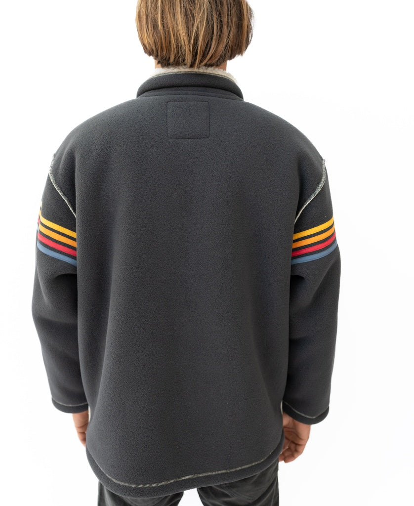 A person stands with their back to the camera, wearing the Golden Breed Reef Bonded Sherpa Jacket in Wash Black, which features multicolored sleeve stripes and cozy polyester sherpa, set against a white background.