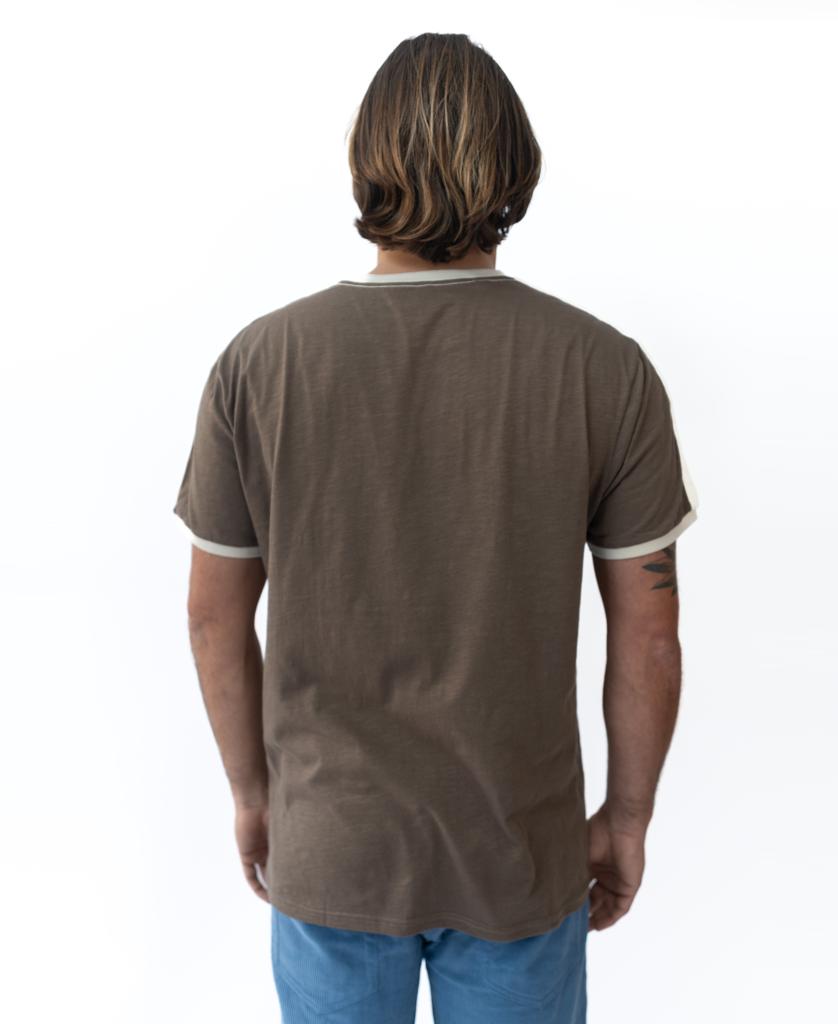 A person with shoulder-length hair, wearing the Golden Breed Retro Ringer Tee in Wash Brown and blue pants, stands facing away from the camera against a white background, channeling classic 70s vibes.