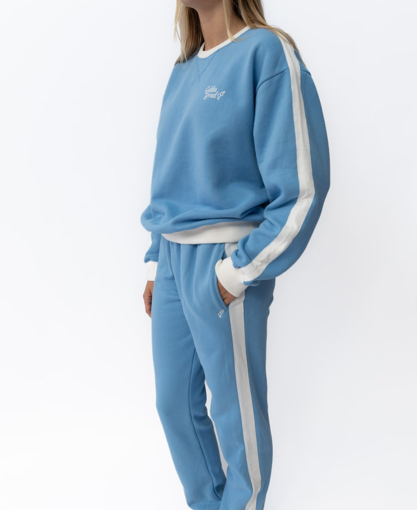 Model wears Golden Breed Retro Crunchie T/P in Azure/Off White, a matching light blue cotton fleece sweatshirt and trackpants set featuring signature Golden Breed Stripe detailing, standing against a plain white background.