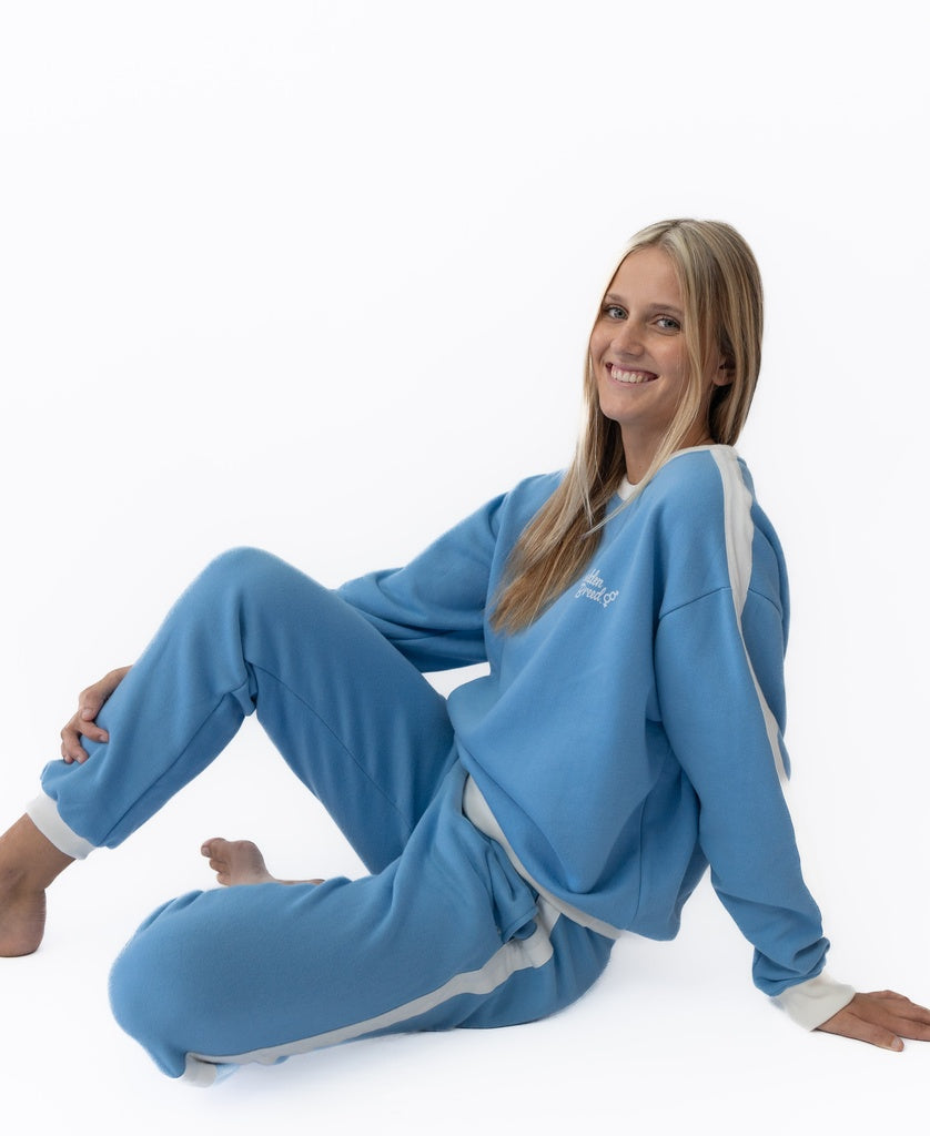 A woman with long blonde hair sits on the floor, smiling, wearing Golden Breed’s Retro Crunchie T/P in Azure/Off White against a white background.