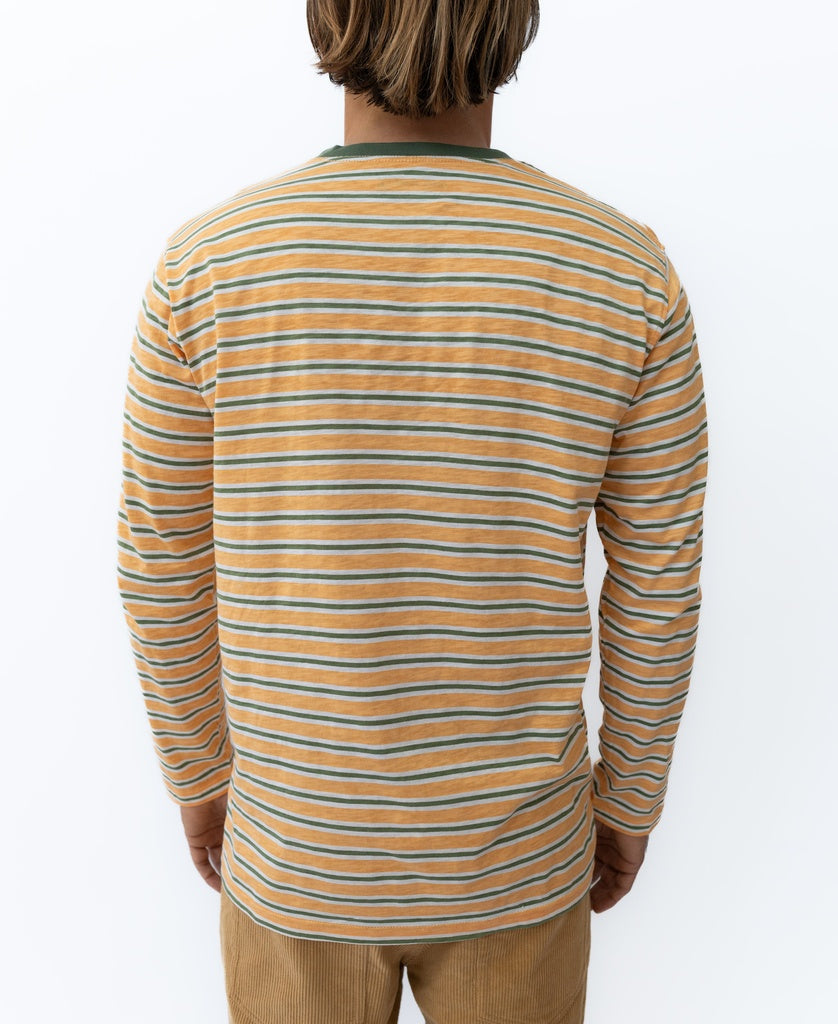 Someone stands facing away, wearing the Golden Breed Rincon Stripe LS Tee | Wash Orange—crafted from soft cotton jersey with orange, white, and green stripes—paired with tan pants.