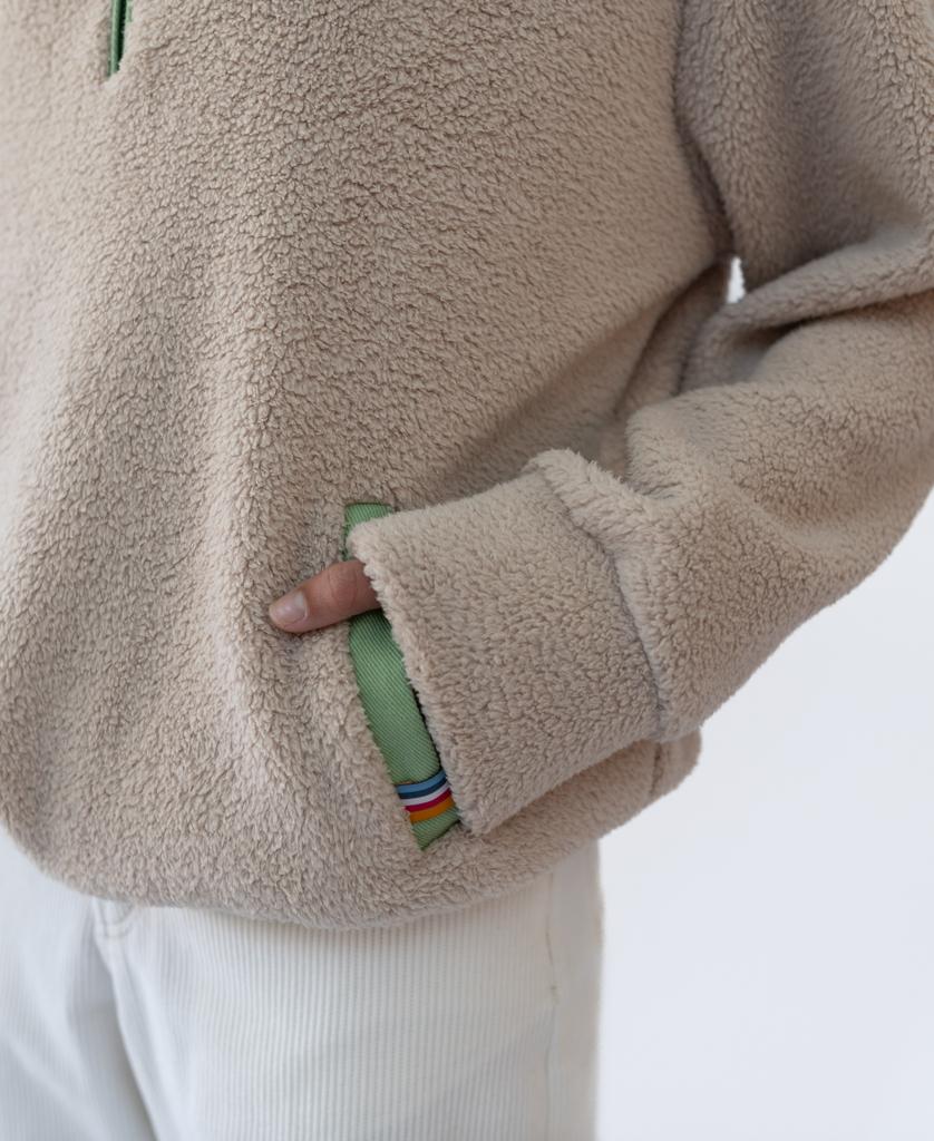 A person wearing the Golden Breed Sammie 1/2 Zip in beige with a green pocket lining, Retro Golden Breed Logo, and white pants, one hand partially in the pocket.