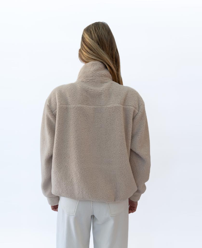 A person with long, light brown hair is shown from behind, wearing Golden Breeds Sammie 1/2 Zip in beige and light-colored pants against a plain white background.