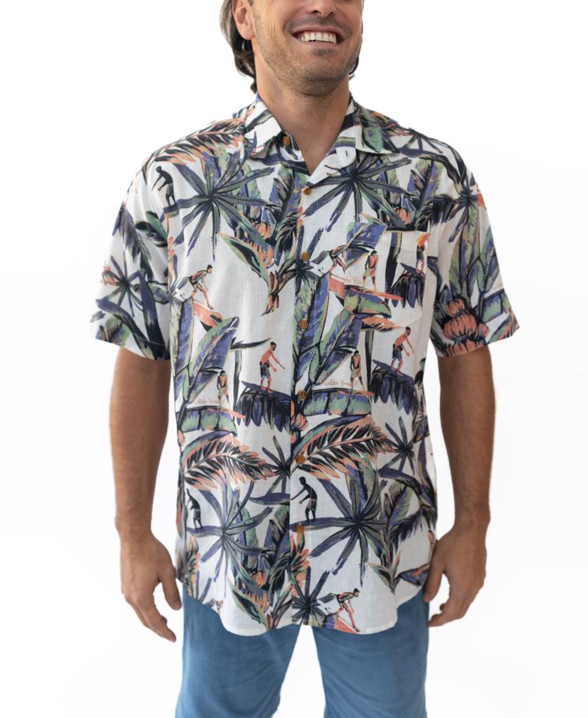 A man wears the Golden Breed Surfer Palm Shirt in Off White, featuring a tropical print cotton/linen blend, paired with light blue pants, standing against a plain white background.