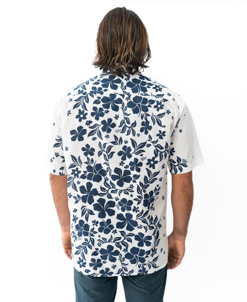A person with shoulder-length hair is seen from the back wearing a white Vomo Floral Shirt by Golden Breed, featuring a blue floral pattern in an oversized relaxed fit, paired with dark pants.