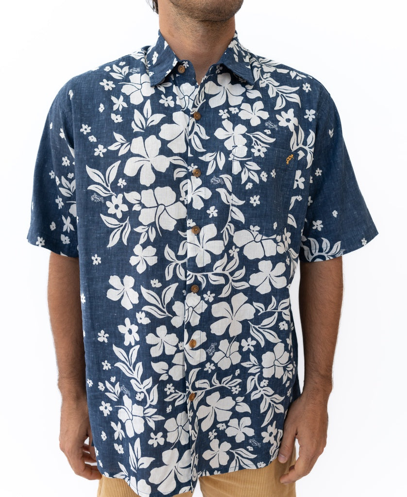 A man wears the Golden Breed Vomo Floral Shirt in vintage navy with a white floral pattern and tan linen pants, standing against a plain white background.