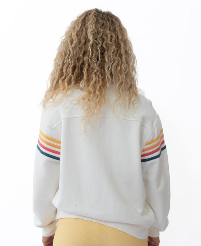 A person with curly hair wears the Golden Breed Long Island 1/4 Zip in Off White, featuring colorful sleeve stripes and yellow shorts, standing with their back to the camera against a white background.