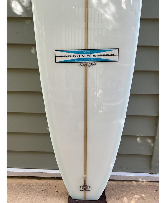 A close-up of the Gordon & Smith G&S 10 Easy Rider Polish Finish longboard surfboard in white, featuring a vertical wood stringer and the classic Easy Rider design.