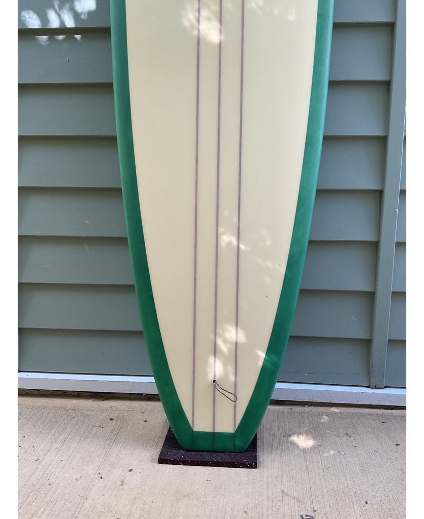 The Gordon & Smith G&S 96 Easy Rider Triple Stringer in Green/Cream stands upright on concrete, showcasing its user-friendly design, triple stringers, and green edges against light green siding.