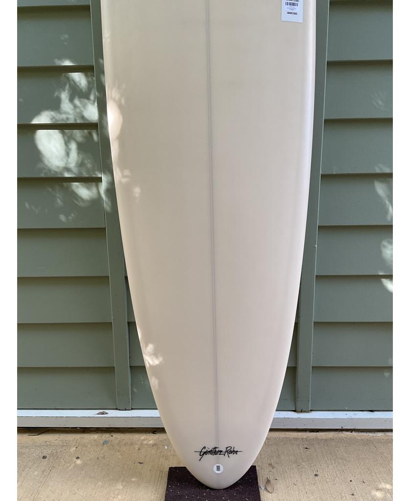 The G&S 78 Cool Tool Mid Twin | Cream surfboard by Gordon & Smith, known for relaxed surfing and great wave catching, stands upright against a green paneled wall with the brand logo near the bottom.