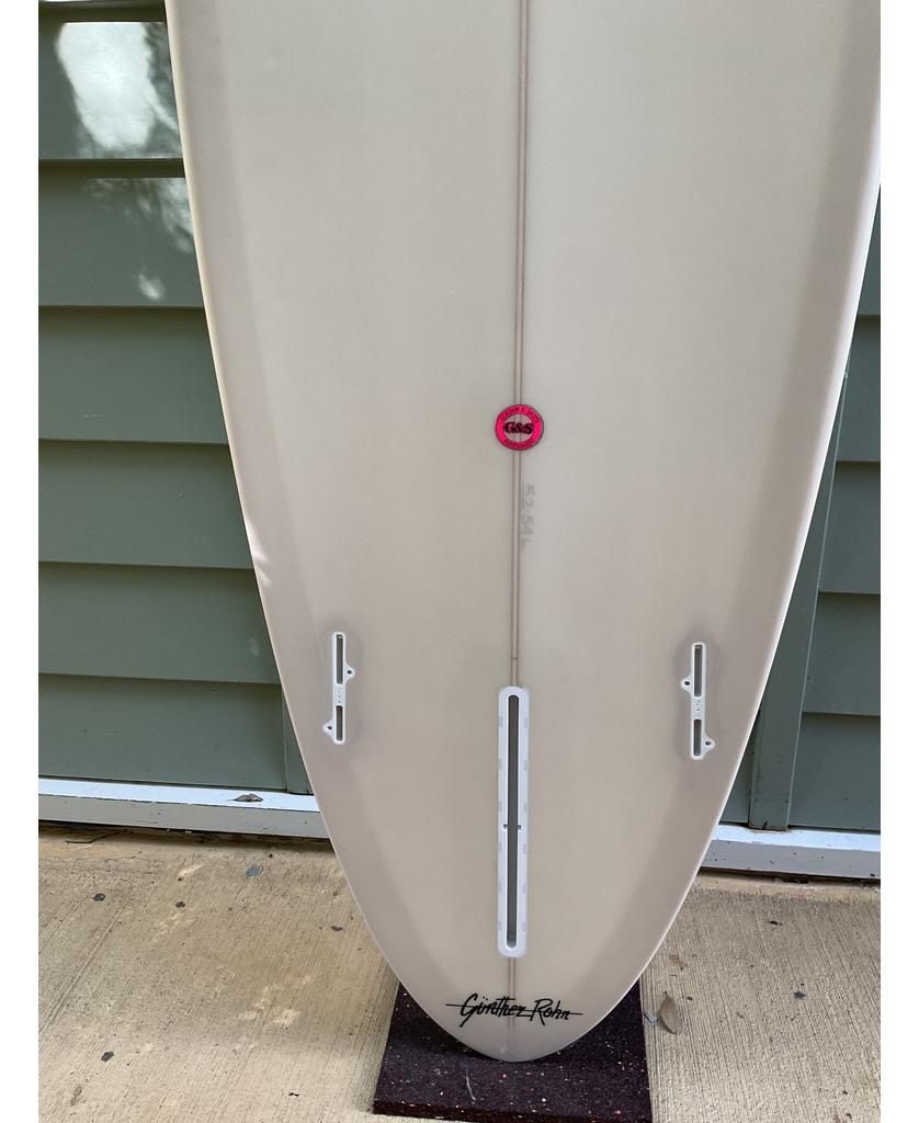 The Gordon & Smith G&S 78 Cool Tool Mid Twin in cream stands upright against a green wall, its three fin boxes ready to boost your wave catching for smooth, relaxed surfing sessions.