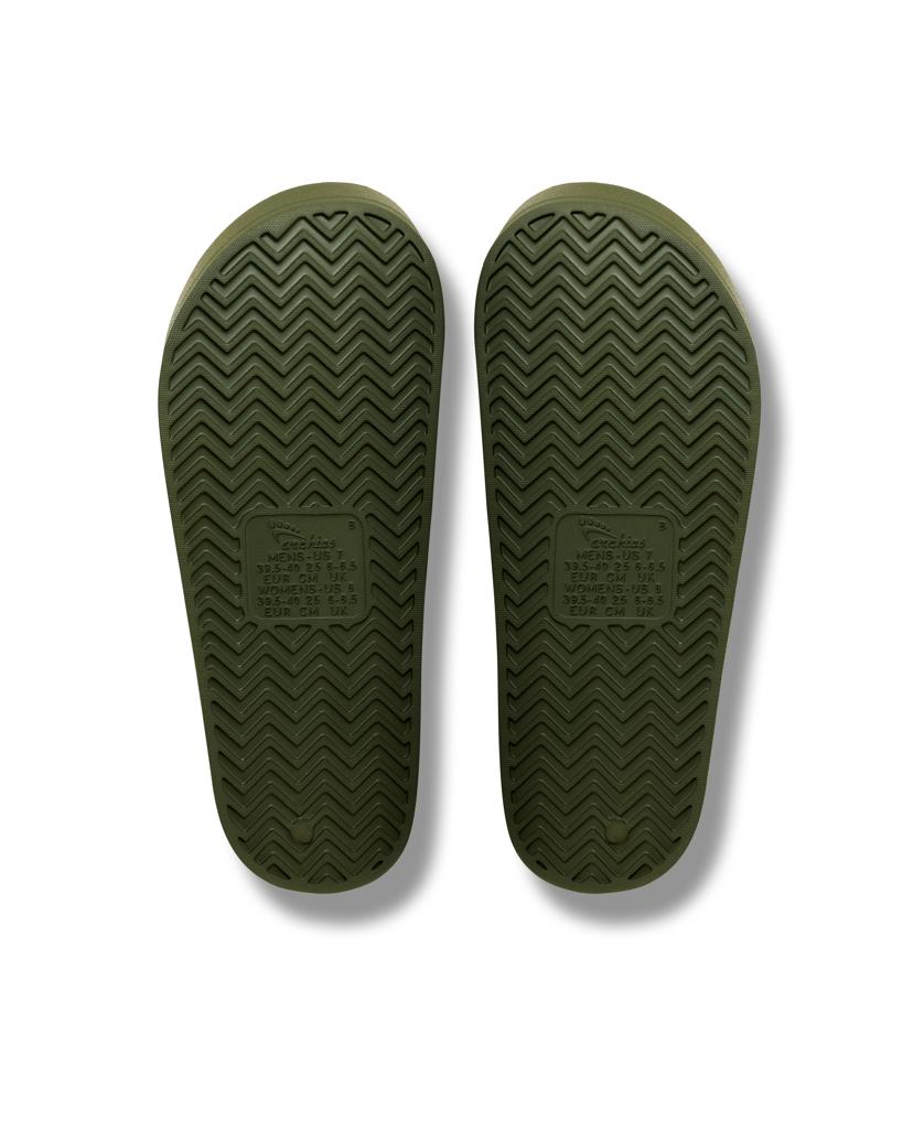 A pair of Archies Archie Slide sandals in khaki, featuring closed cell foam soles with a herringbone tread pattern, shown from the bottom on a white background.