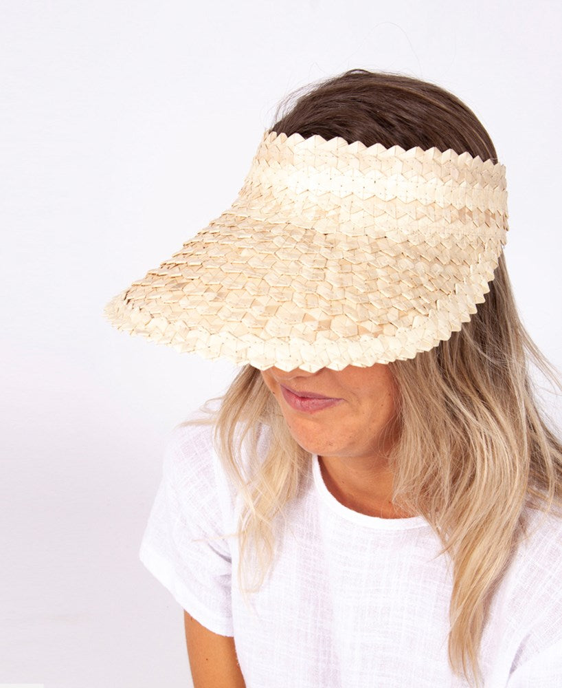 A person wearing the Lazy Beach Palm Visor | Natural, made from 100% palm leaf, and a white shirt faces slightly downward against a plain white background.