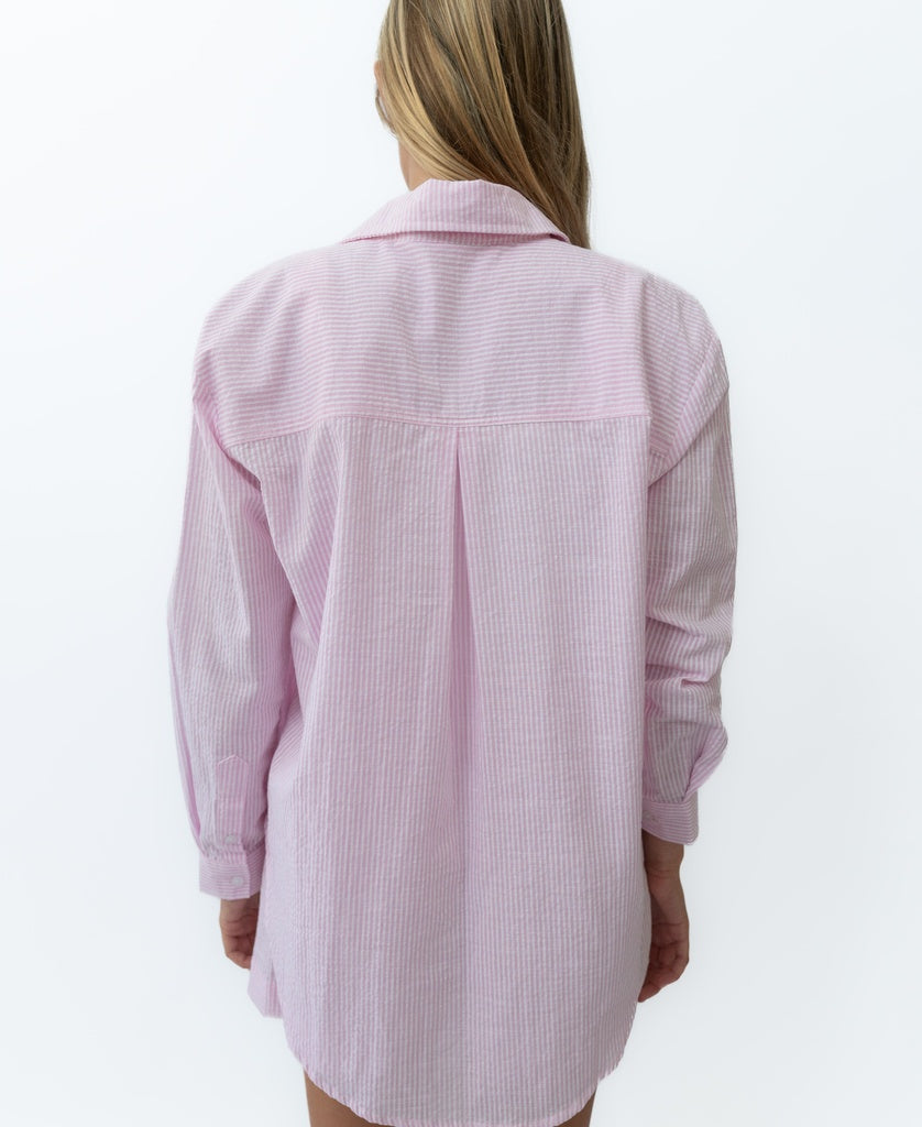 A person with long hair is seen from the back wearing the Lazy Beach Maeve L/S Shirt in baby pink stripe, made from cotton seersucker, against a plain white background.
