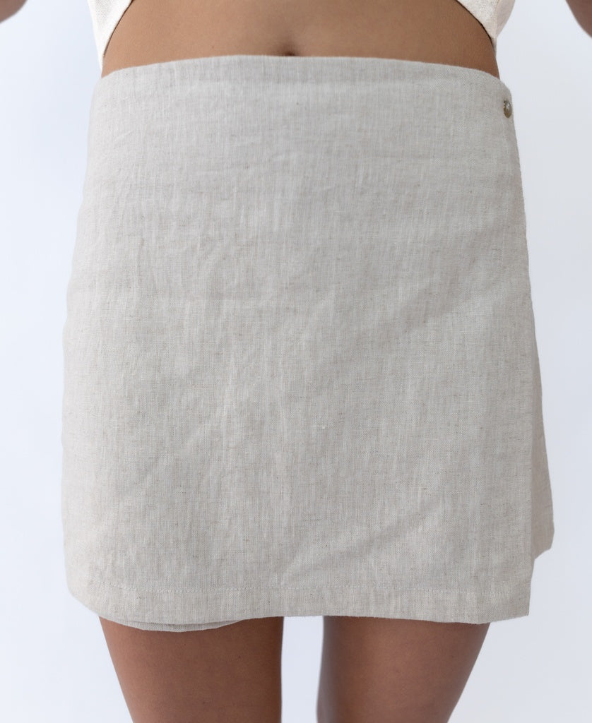 A person wears the Lazy Beach Indiana Skort Linen in Natural, made from 100% linen with a subtle waistband button detail, shown from waist to mid-thigh.