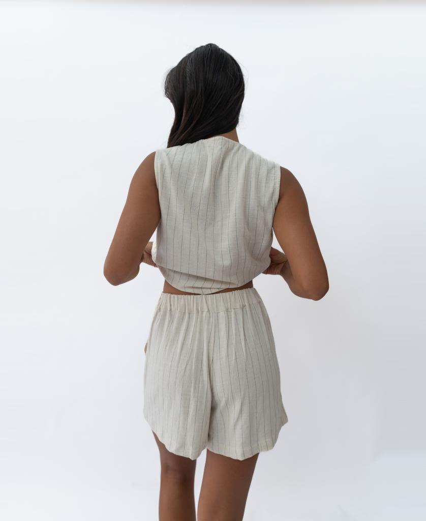 A person with long dark hair wears the Lazy Beach Kris Short in Off White Fine Pinstripe, paired with a sleeveless top, standing against a plain white background for a chic summer look.