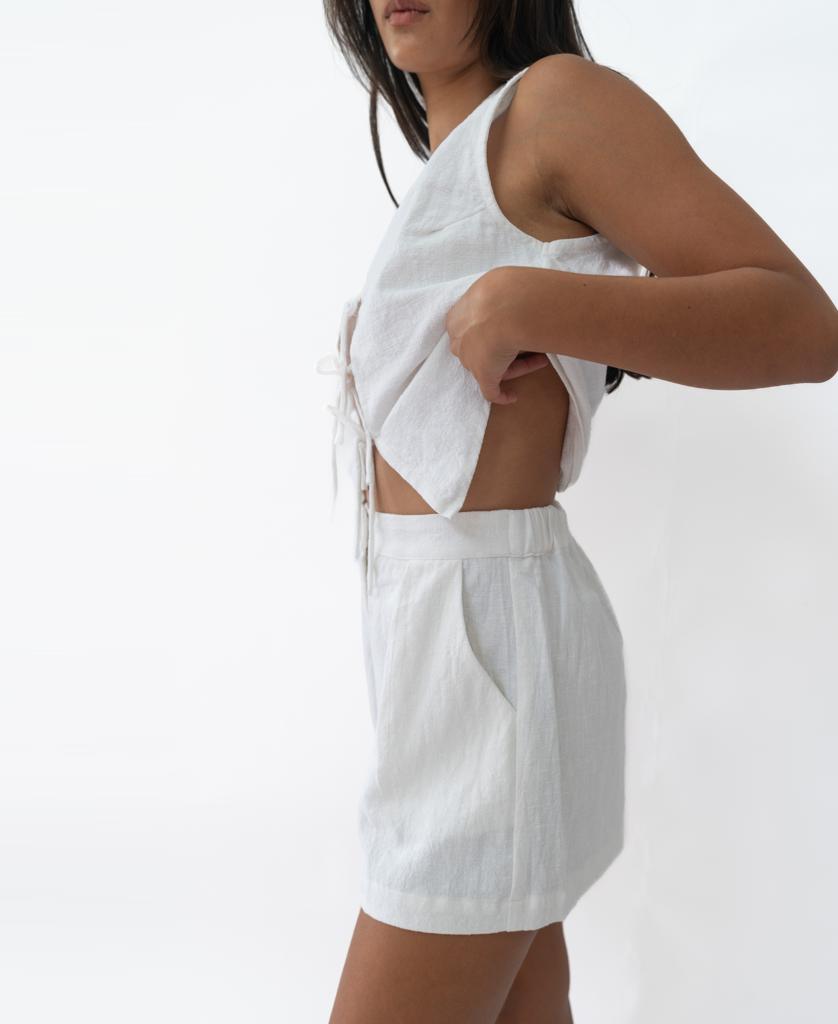 A person wearing Lazy Beachs Kris Short in white, handmade in Bali, pairs it with a sleeveless white linen top and stands against a plain white background.