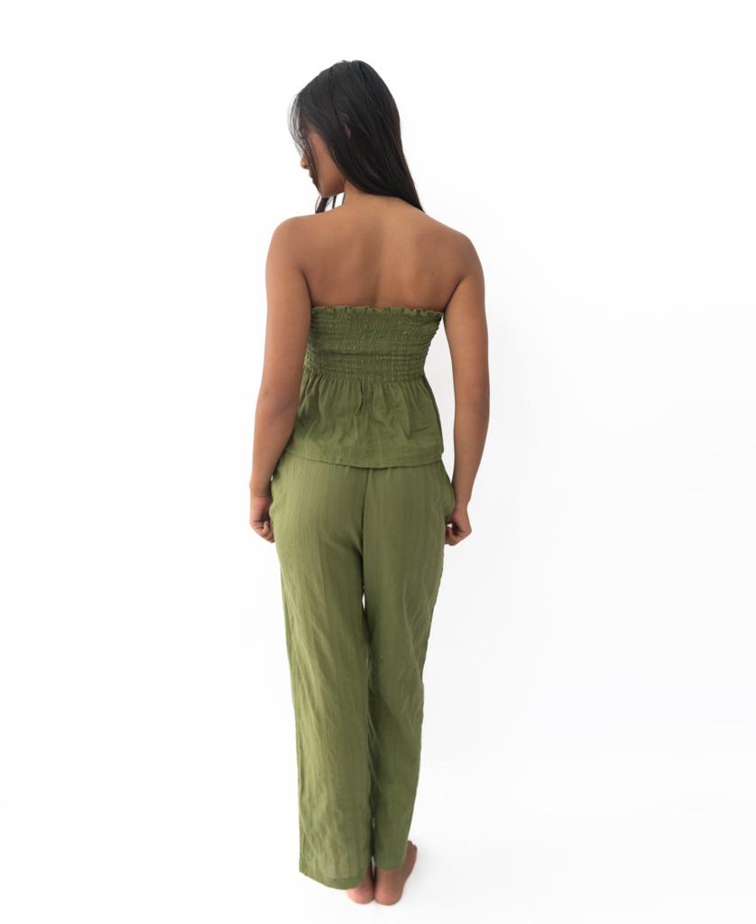 A woman stands barefoot facing away, wearing Lazy Beachs Liberty Pant in khaki—straight leg with an elastic waist—paired with an olive green strapless top, all made from soft cotton, set against a plain white background.