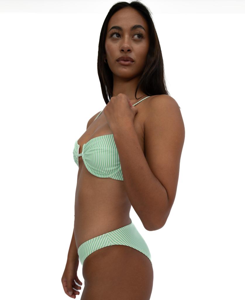 A woman poses against a plain white background, wearing the Lazy Beach Millie Bottom in Green / White Stripe—crafted from sustainable Italian fabric—and looks slightly to the side.