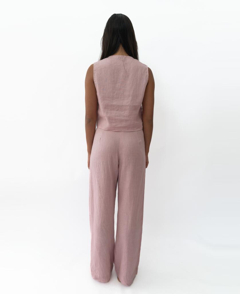 A woman faces away from the camera, wearing the Rennie Vest in blush linen by Lazy Beach—an ideal sleeveless summer piece—against a plain white background.