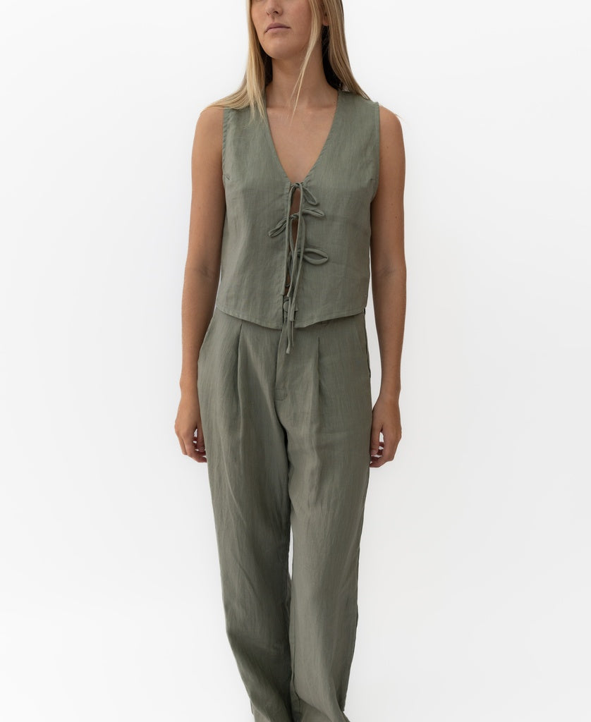 A woman wears the Lazy Beach Rennie Tie Vest Linen in dark khaki with matching high-waisted pants, handmade in Bali, standing against a plain white background.