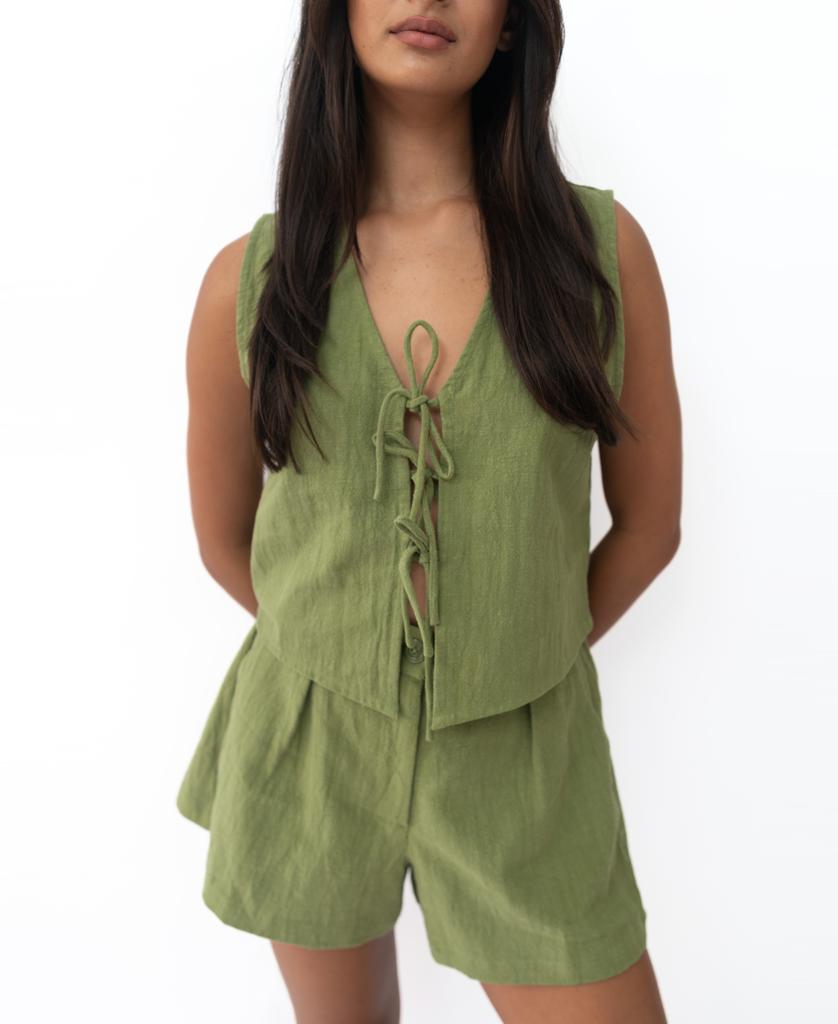 A woman wears the Lazy Beach Rennie Vest in Khaki—sleeveless with a lace-up front—paired with matching shorts, handmade in Bali, standing against a plain white background.