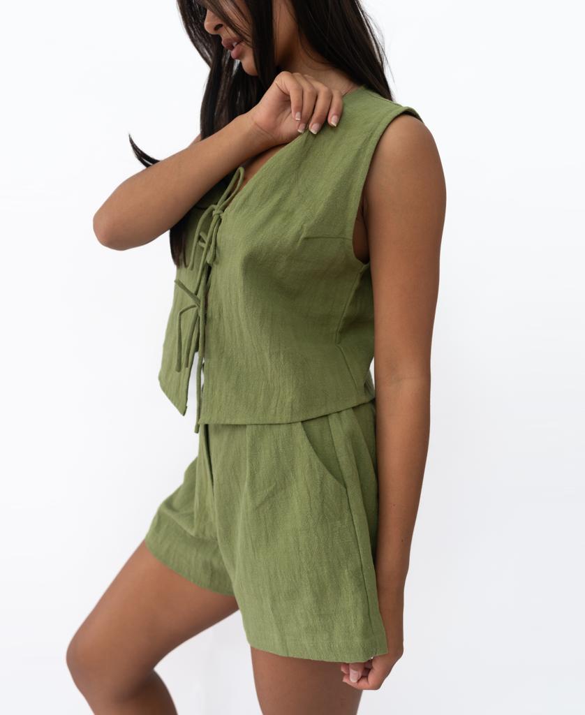 A woman stands against a plain white background wearing the Lazy Beach Rennie Vest in khaki, a handmade sleeveless two-piece set from Bali featuring a front tie top and matching shorts.