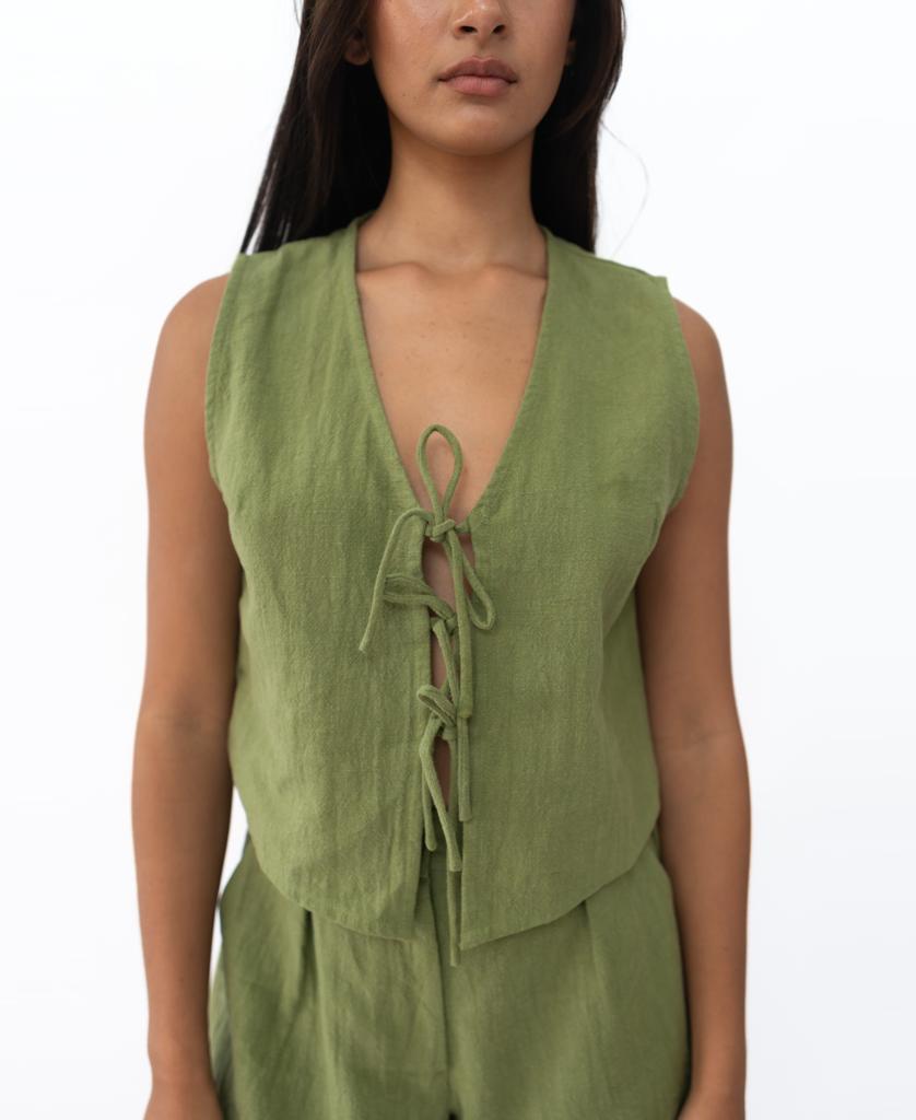 A person wears the Lazy Beach Rennie Vest | Khaki, a sleeveless vest with a deep V-neck and three front ties, paired with matching pants. Handmade in Bali, theyre standing against a plain white background.