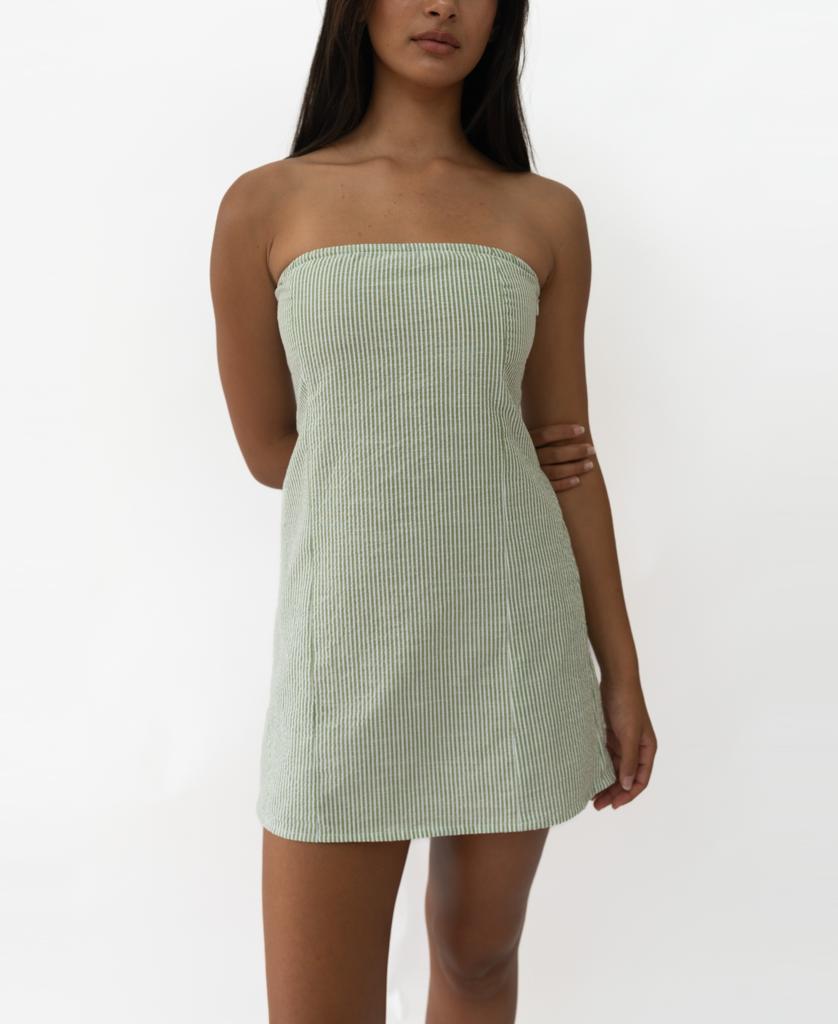 A woman wearing the Lazy Beach Victoria Dress in Olive Stripe—a mini strapless dress—stands against a plain white background.