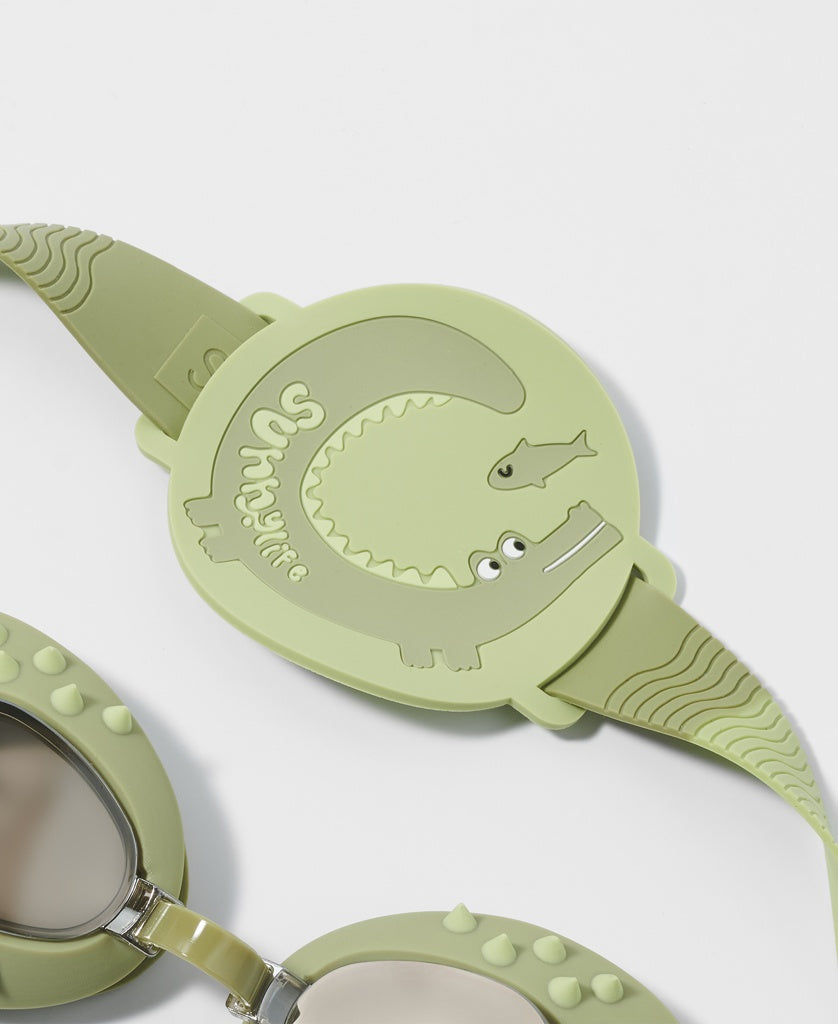 A close-up of Sunny Life Kids Swim Goggles Cookie the Croc in khaki, featuring a crocodile design on the strap and anti-fog lenses for clear underwater vision.