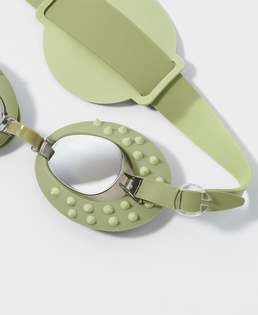 A pair of Sunny Life Kids Swim Goggles Cookie the Croc in khaki, featuring mirrored anti-fog lenses and textured bumps around the frames, is displayed on a white surface.