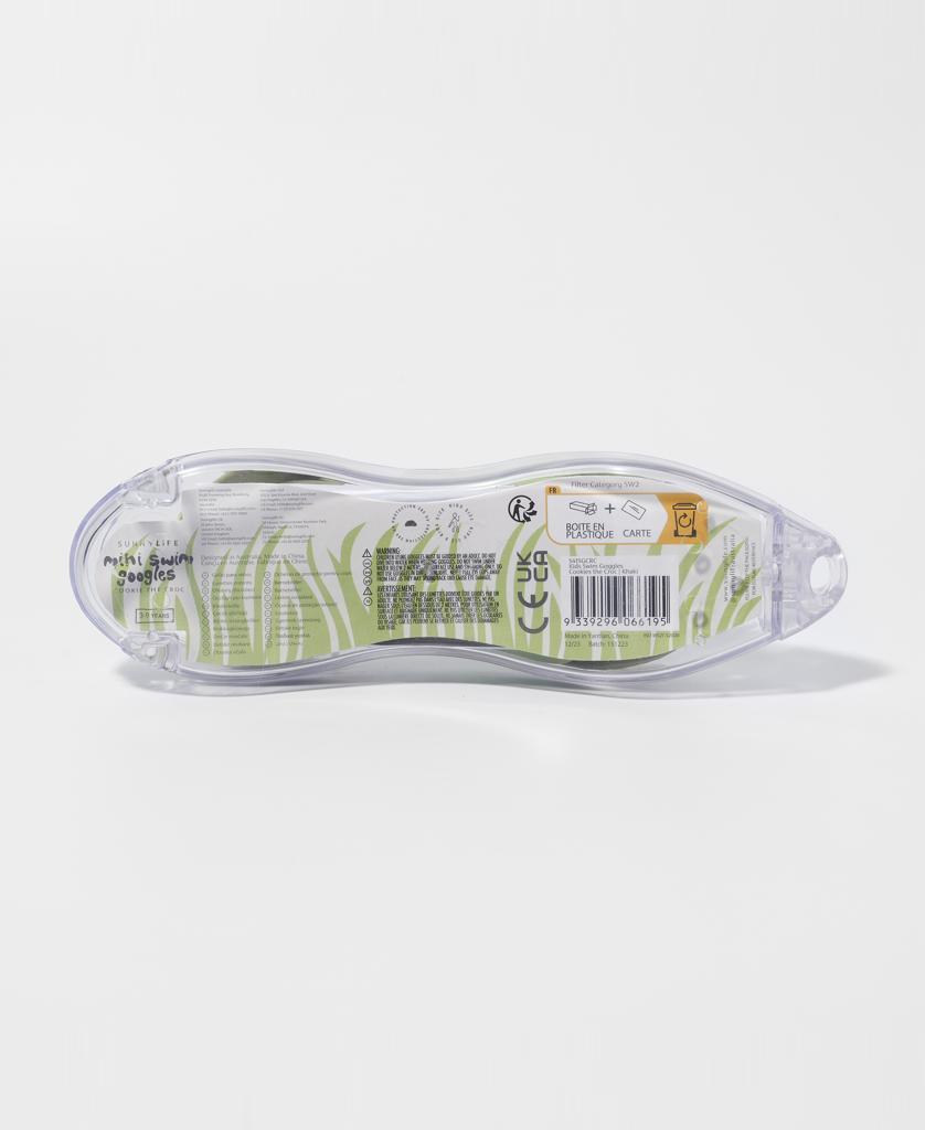 A clear plastic container with a green and white label holds Sunny Life Kids Swim Goggles Cookie the Croc | Khaki, featuring anti-fog lenses. The back shows a barcode and text, all photographed against a plain white background.