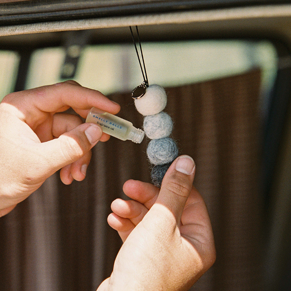 A person uses Smelly Balls Rugged Set Tobacco Vanilla fragrance oil on wool felt balls, hanging as a diffuser inside their vehicle.