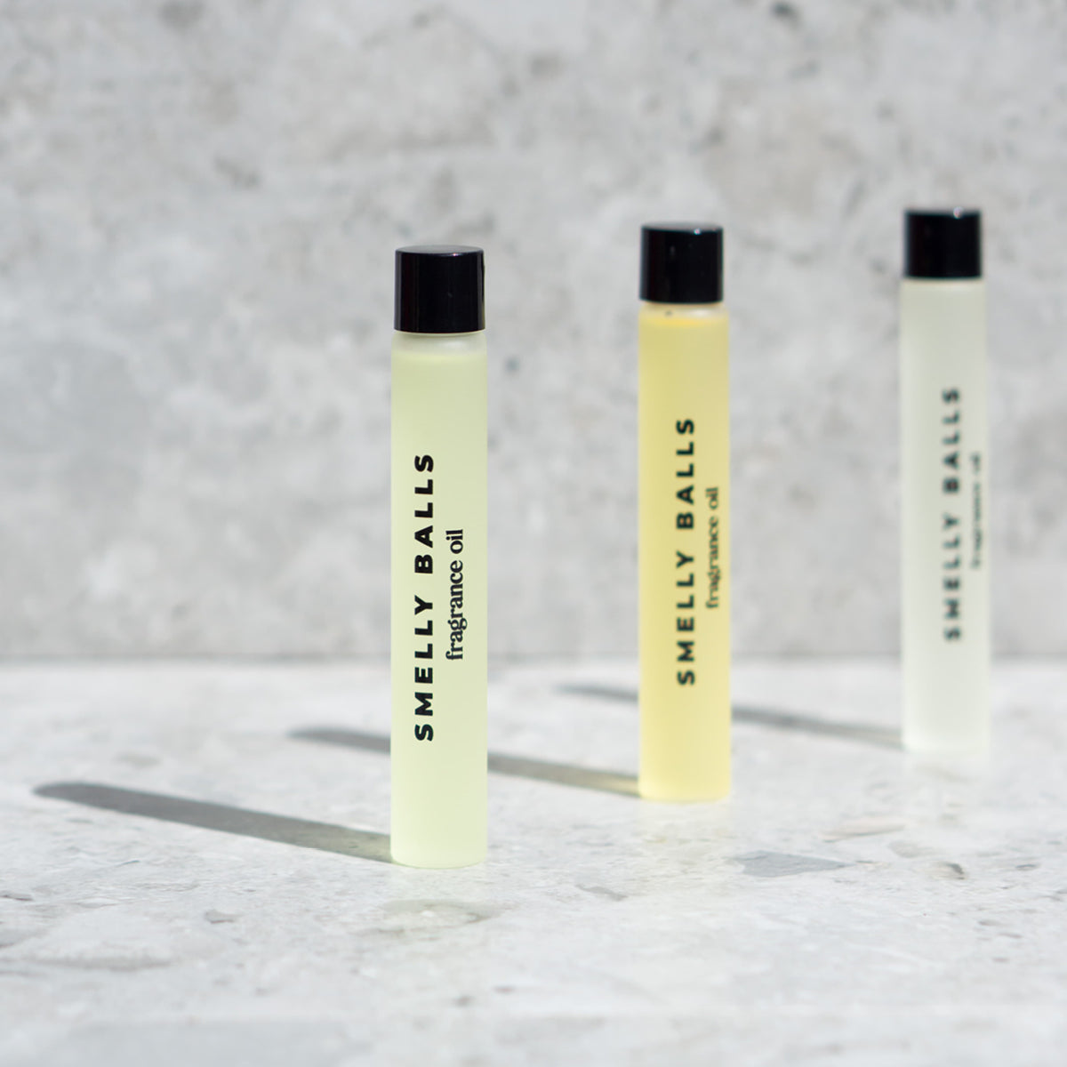 Three small glass vials of Smelly Balls Coastal Drift Fragrance Oil with black caps stand on a light stone surface, ready to infuse your space with a refreshing ocean breeze scent.